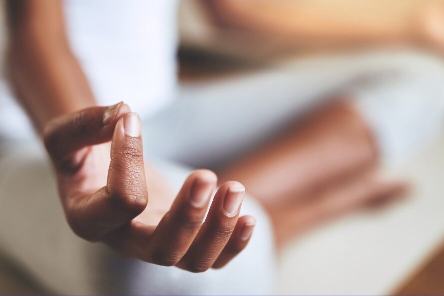 A person sitting in a meditation position with their hand in position of a mudra.