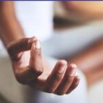 A person sitting in a meditation position with their hand in position of a mudra.