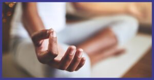 A person sitting in a meditation position with their hand in position of a mudra.