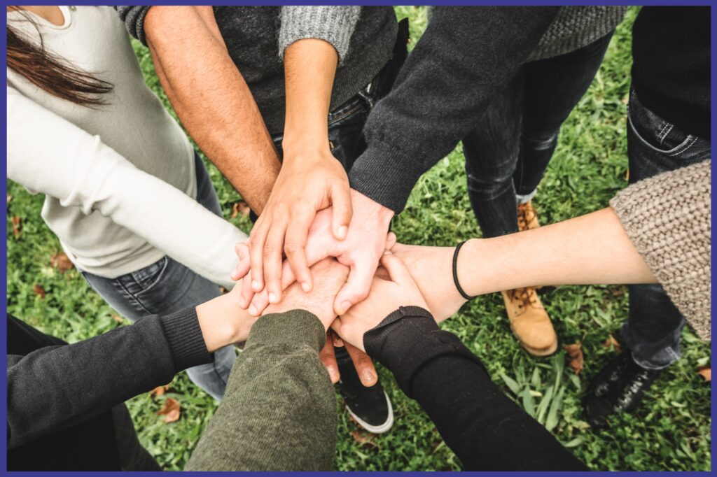 A group of people standing in a circle with everyone holding hands in the center of the circle.